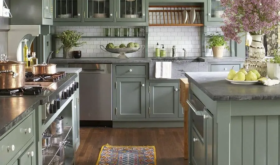 A kitchen with desaturated green cabinetry, gray countertops, white tile, and stained wood